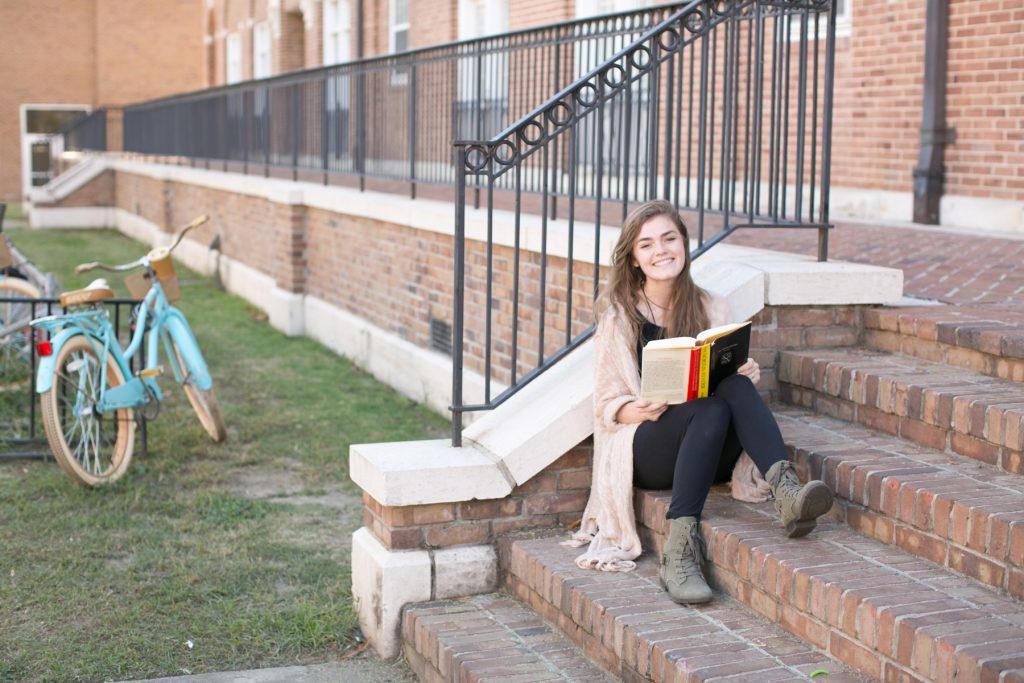 Woman sitting on steps outside with a book