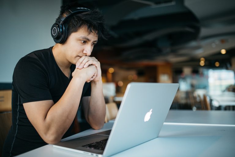 A man looks at a laptop in a cafe while wearing headphones
