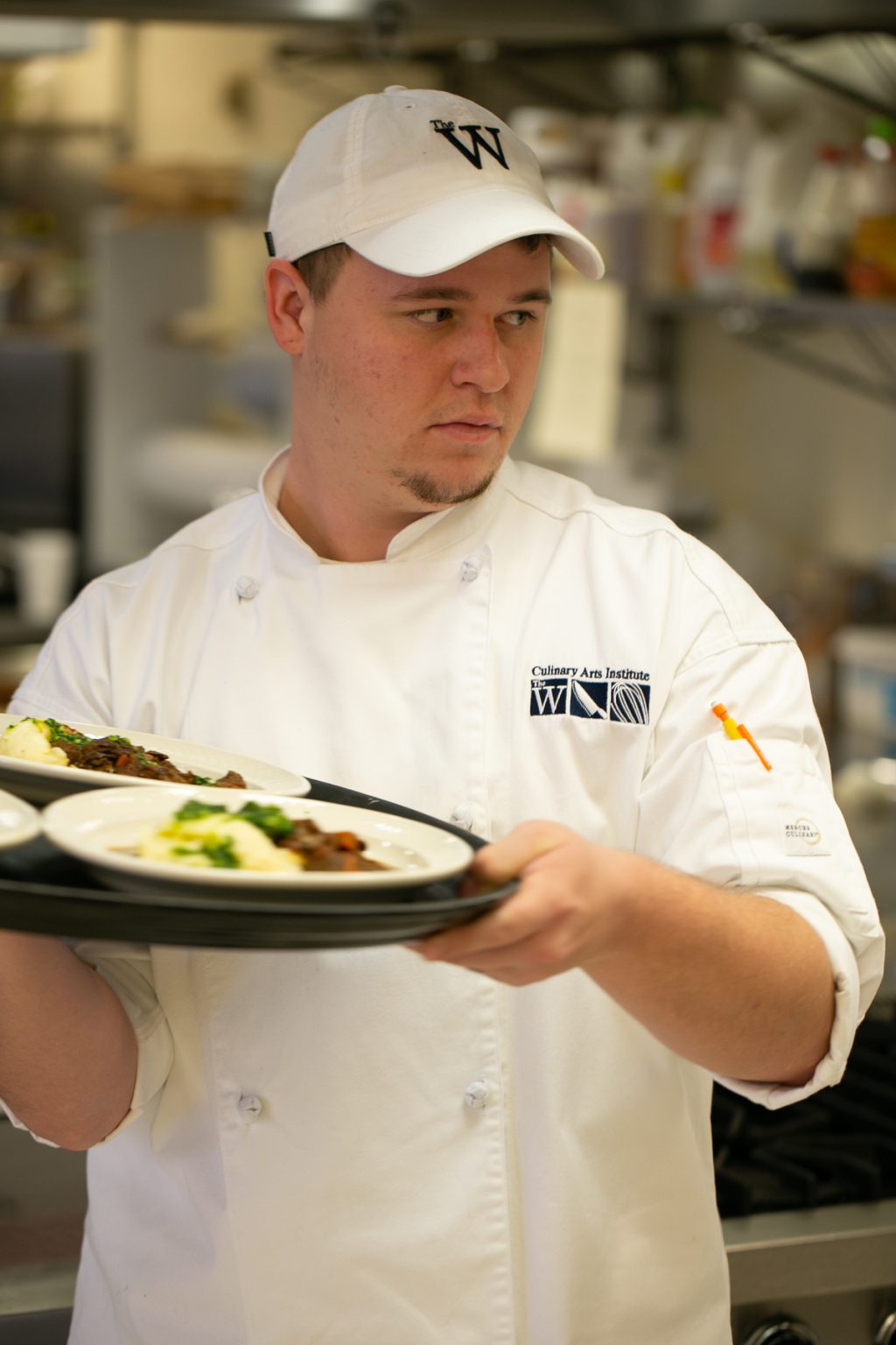 A male student chef carries a tray of plates