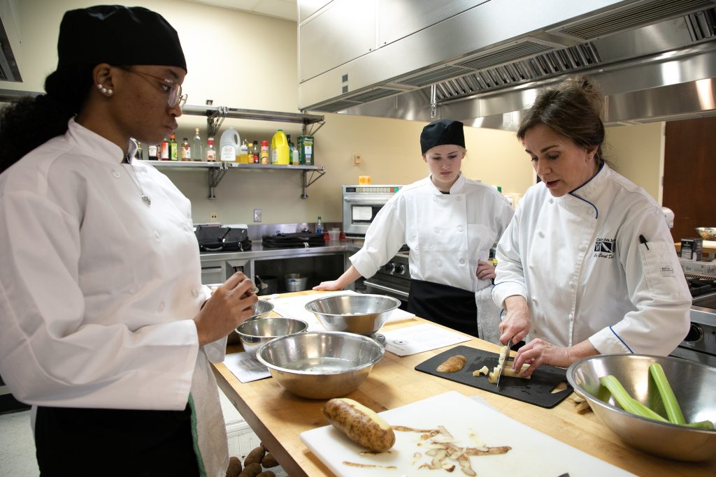 A chef instructors two students in the kitchen