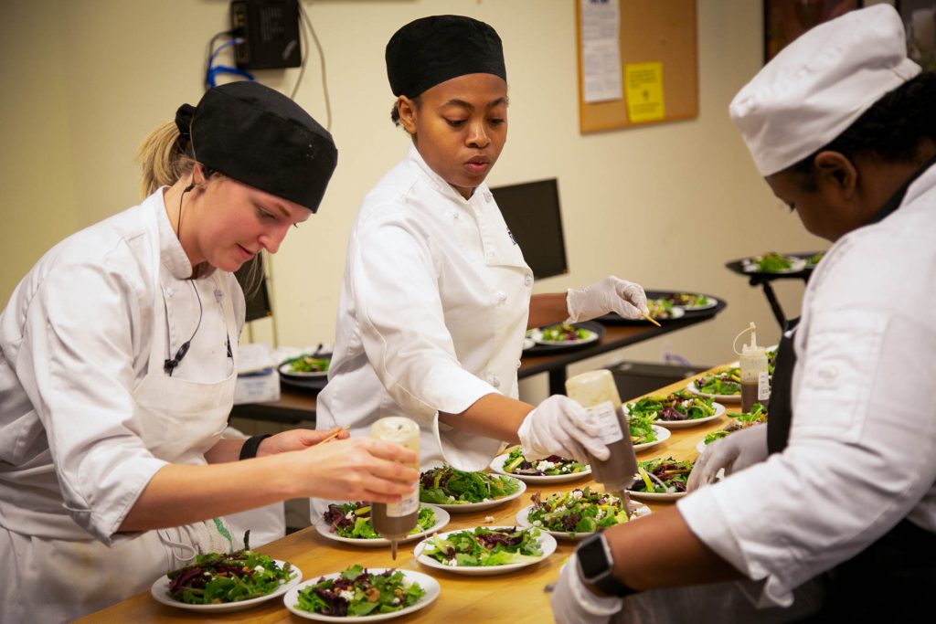 A female student chef plates several salads