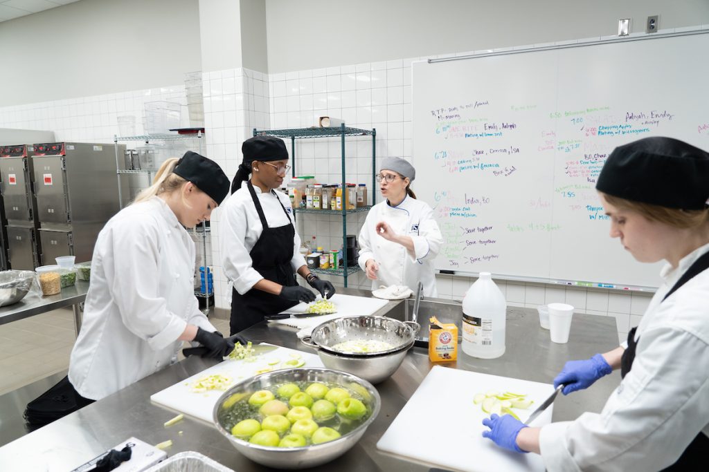 A chef instructs student chefs as they chop apples.