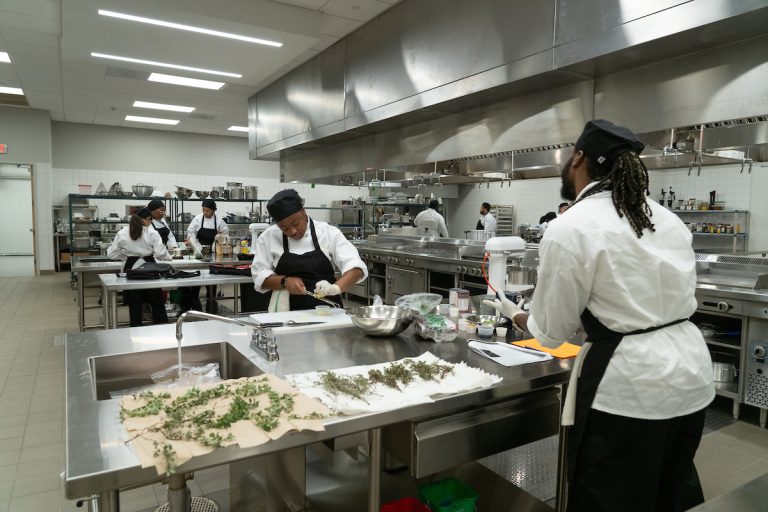 Two student chefs stand in front of prepared herbs