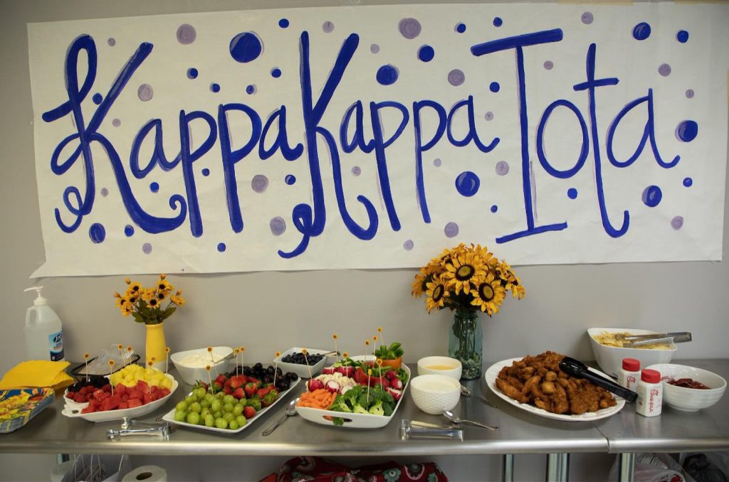 A hand-painted sign reads Kappa Kappa Iota in front of a table of snacks