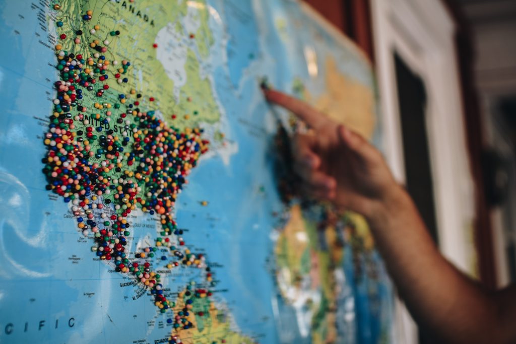 Hand pointing at a world map with hundreds of pins in it.
