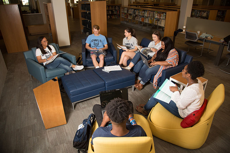 students seated in a circle with books and laptops