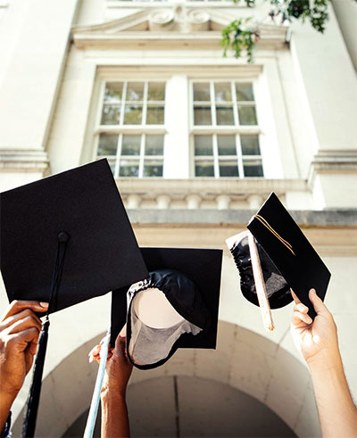 three students raise graduation caps above their heads
