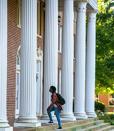 A student walk through columns into Reneau Hall