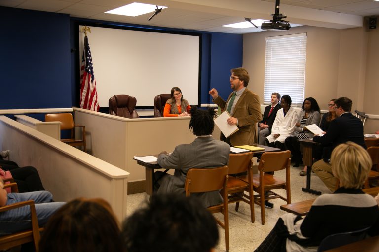 A male student cross-examines a witness during a mock trial