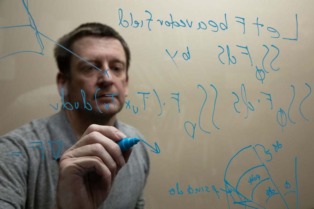 professor writes out a math equation on a board