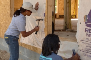 two women hammer on a home construction