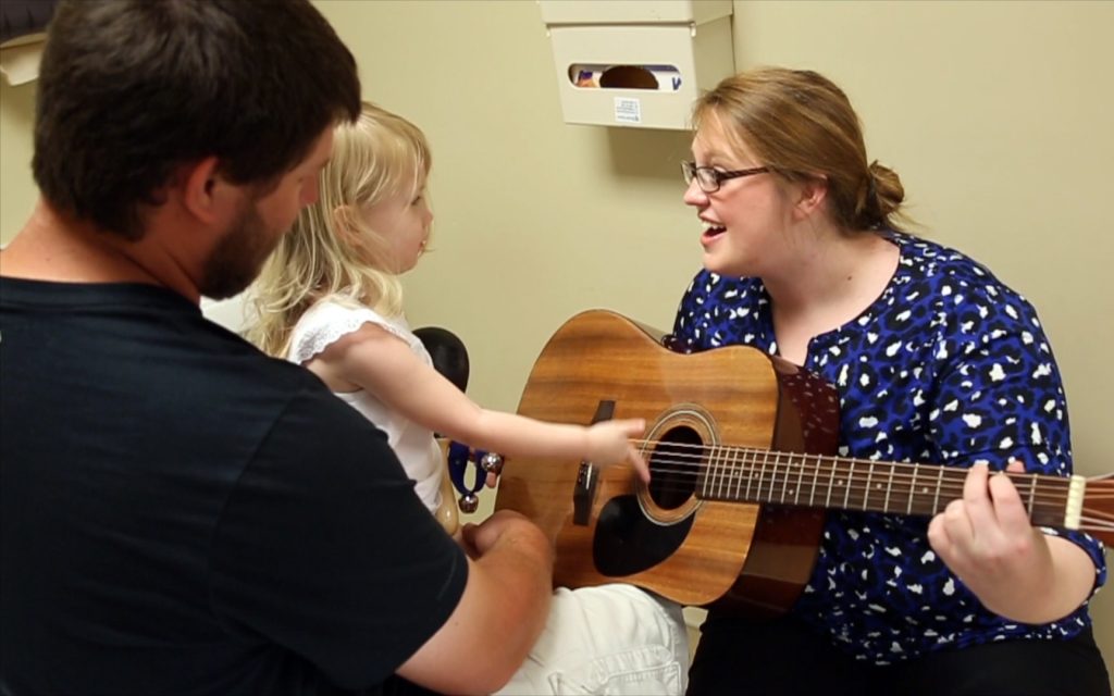 Woman holds guitar in clinic while child plays