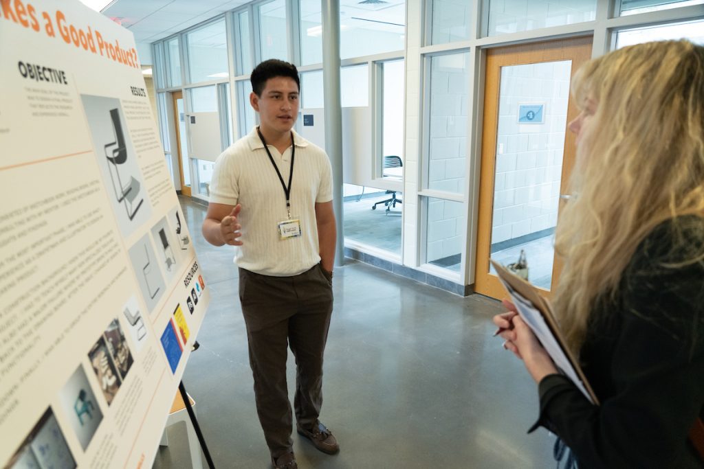 Male student stands next to his research poster