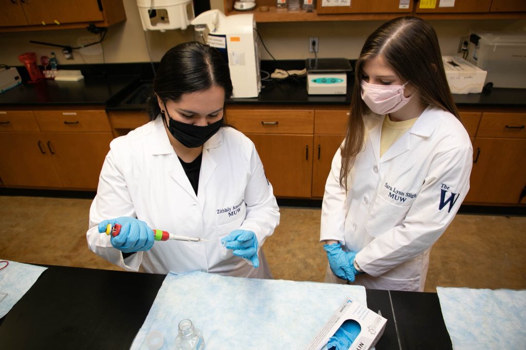Two female students in lab coats examine a specimen in a lab