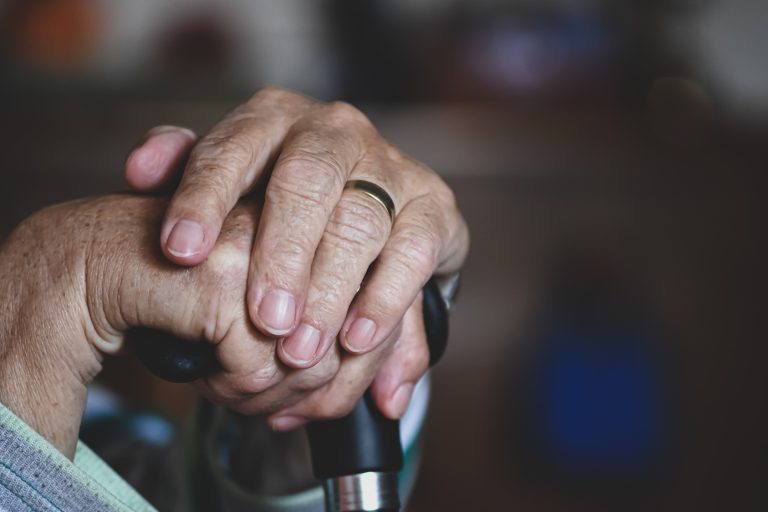 Close up of older person's hands holding a cane