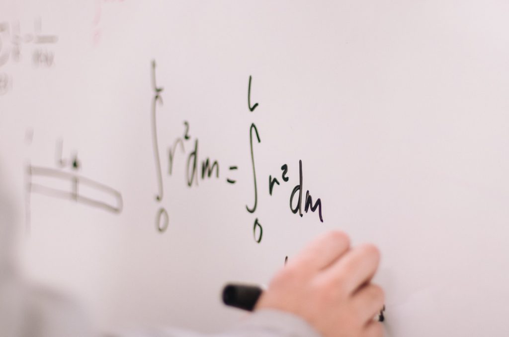 A hand writes a math equation on a whiteboard