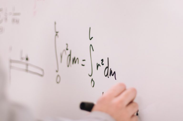 A hand writes a math equation on a whiteboard