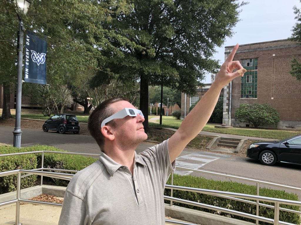 Dr. Hanes, wearing protective solar glasses, pointing at the sun.
