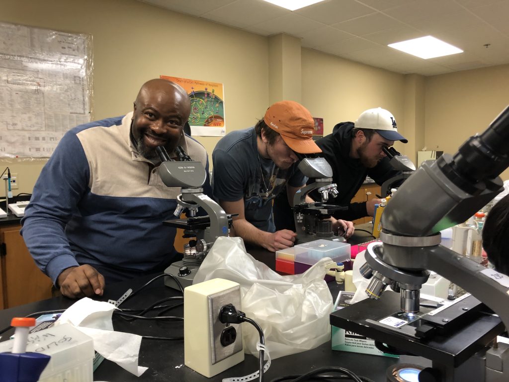 Dr. Onyeagucha at a microscope with students also at microscopes.
