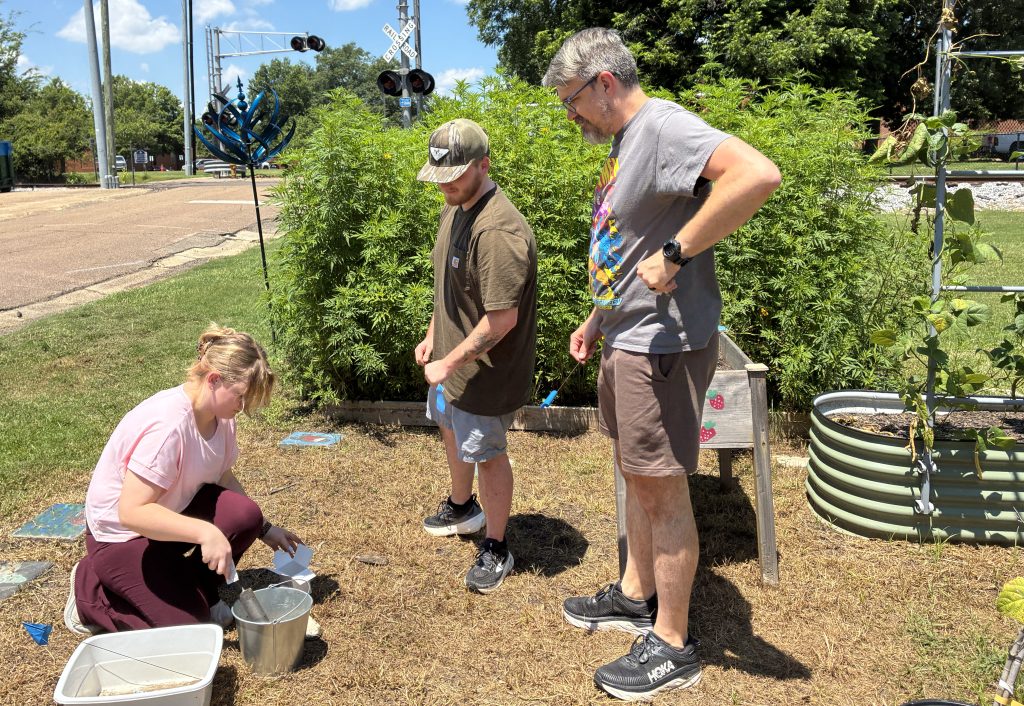 Savannah Voigt digging up dirt samples while Jackson Thompson and Dr. Dodson watch.
