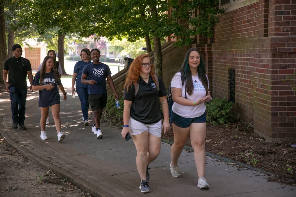 A group of students, 5 women and 3 men, walk past historic Callaway Hall