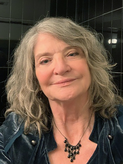 White woman with long curly blond hair, black shirt and necklace