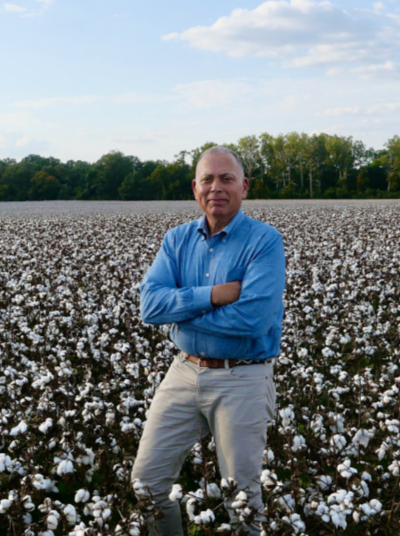 Black an with short hair standing in cotton field wearing khaki pants and light blue shirt