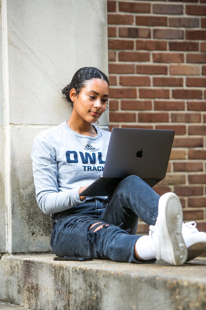 Woman in Owls shirt works on a laptop outdoors