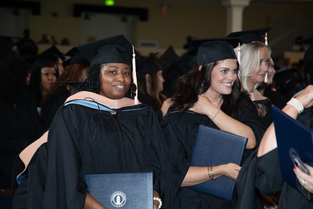 Graduates in their caps and gowns hold their diplomas and smile.