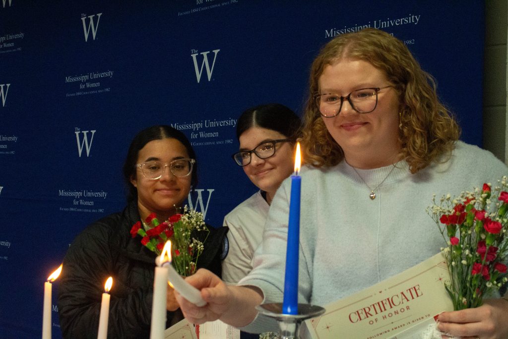 Students light a candle while standing in front of a MUW backdrop