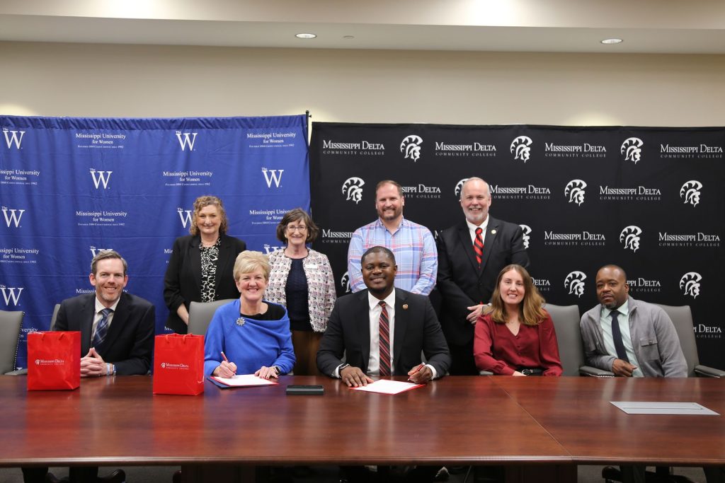 Representatives from The W and MDCC are pictured in front of banners for the two schools during the signing of a Memorandum of Understanding between the two