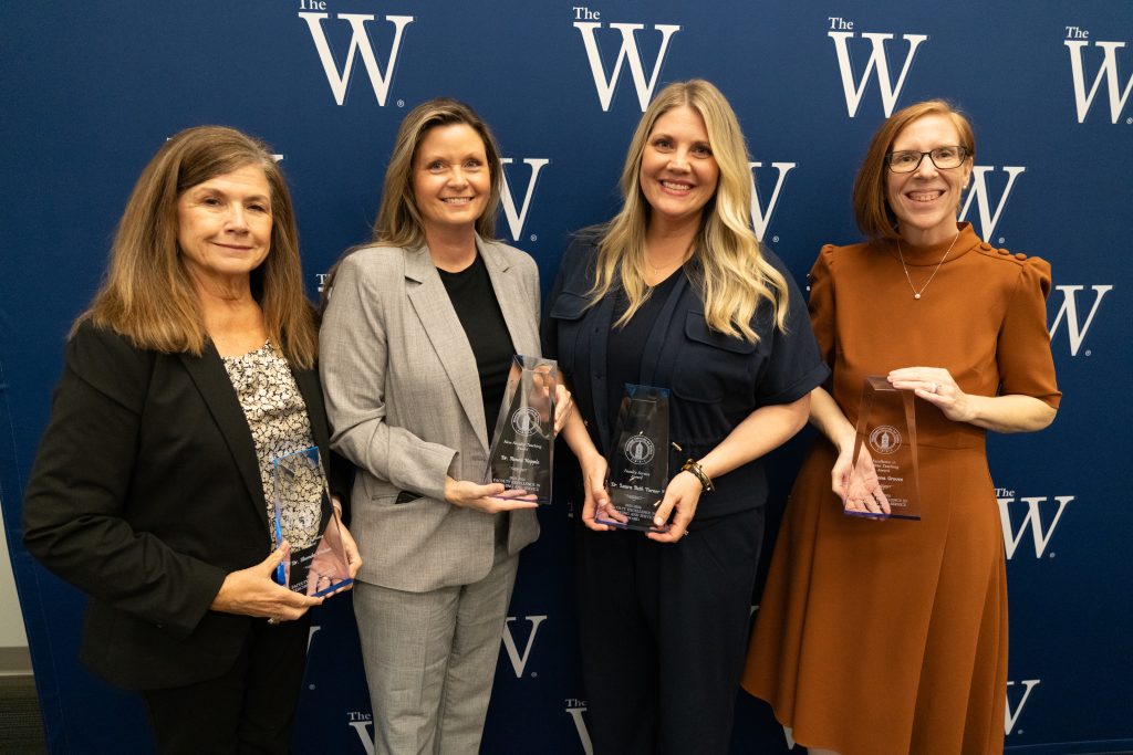 Faculty Excellence Award winners from the department of graduate nursing stand in front of a W backdrop with their trophies.