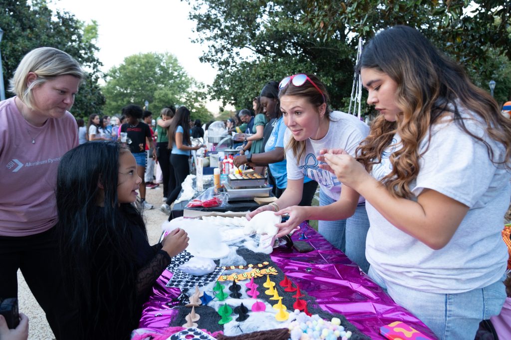 A little girl talks with W students at a table at Oktoberfest 2025.