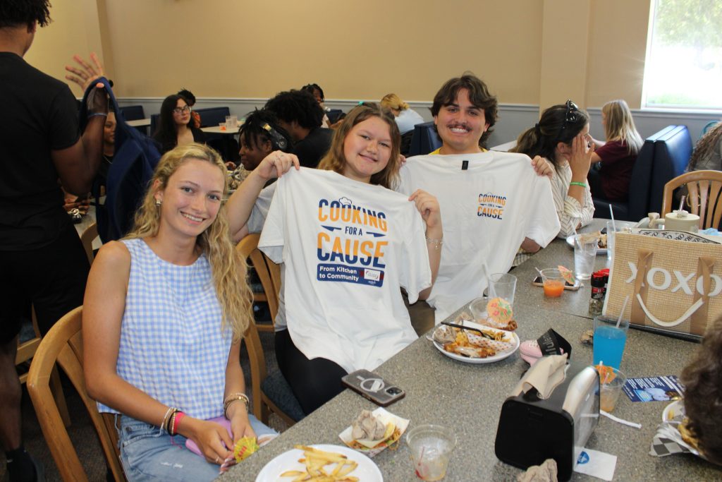W students have their photo taken with a Cooking for a Cause t shirt
